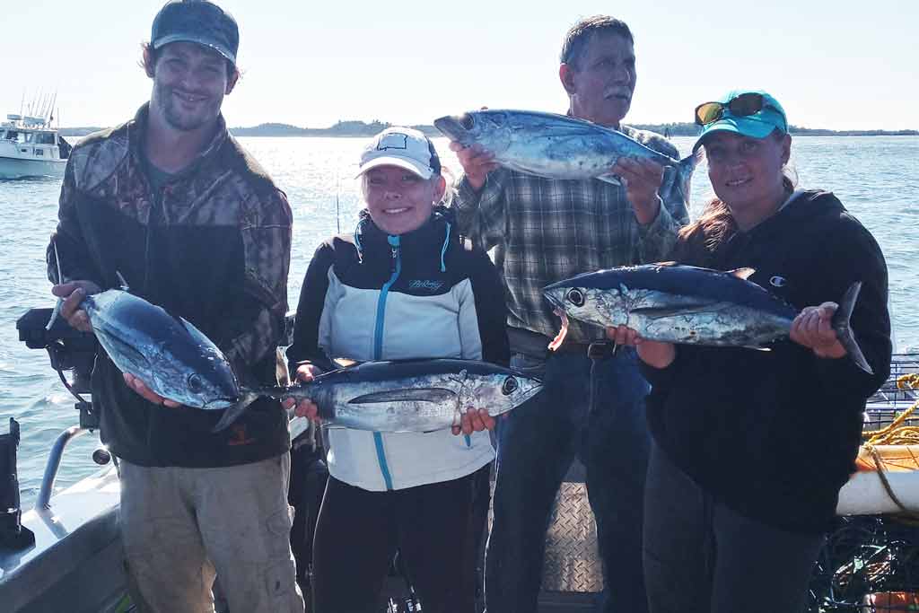 A group of people standing on a boat holding four Albacore Tuna