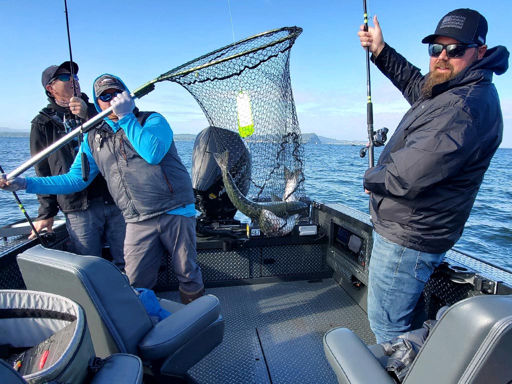 Three anglers on a boat in the process of netting a fish during an angling trip out of Astoria.