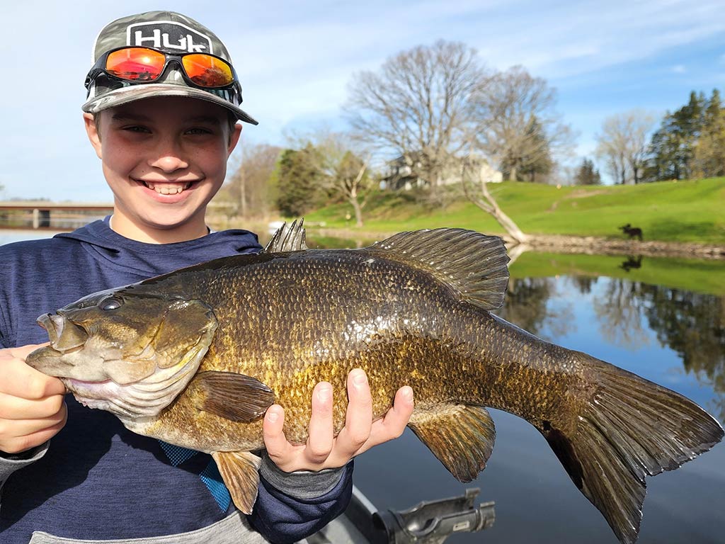 A smiling young angler holding a Smallmouth Bass caught in the Salmon River