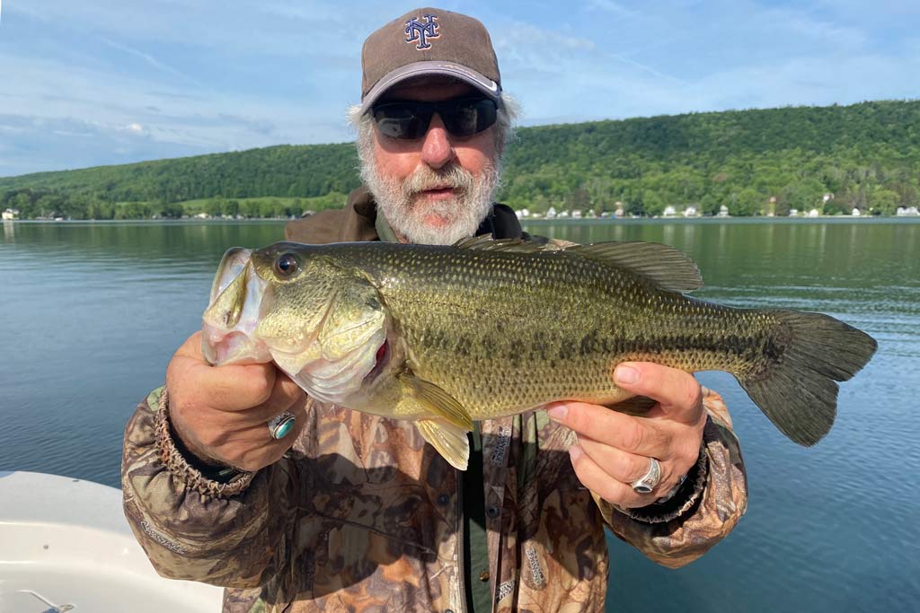 A middle-aged man holding a Largemouth Bass, with a lake behind him