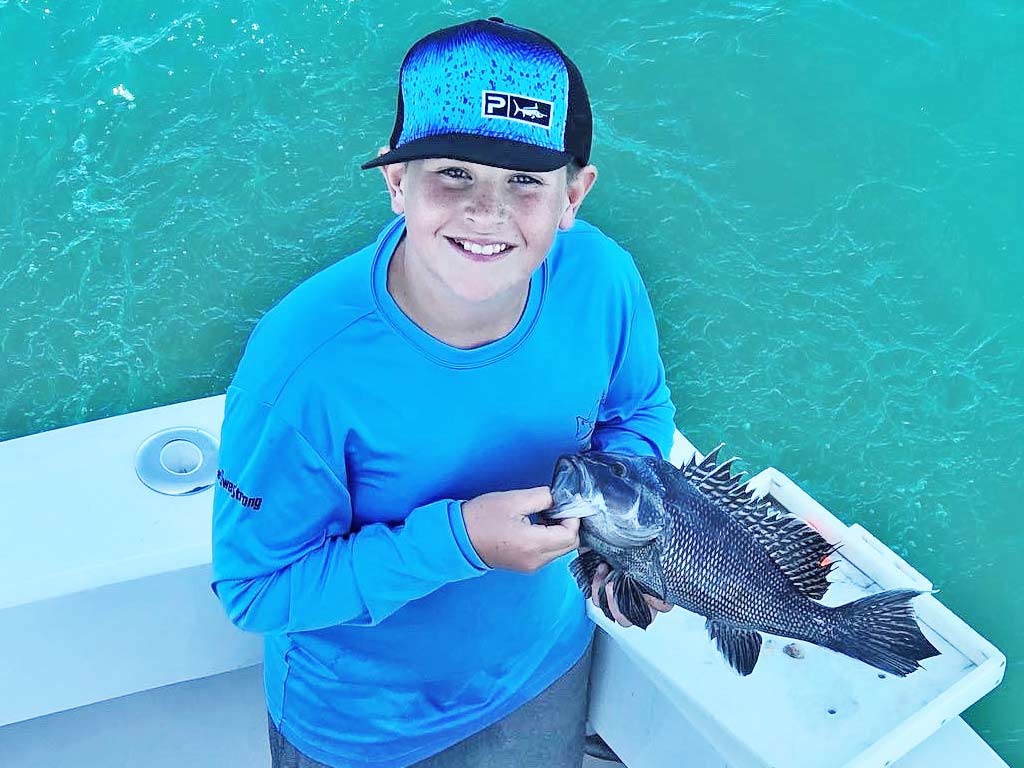 A boy posing for a photo with a Black Seabass he caught.