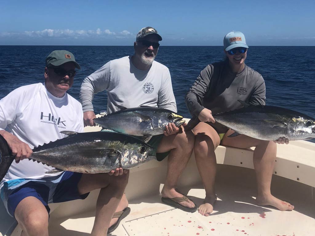 A group photo of three anglers sitting on a Tarpon Springs charter boat and holding their Tuna catches with both hands