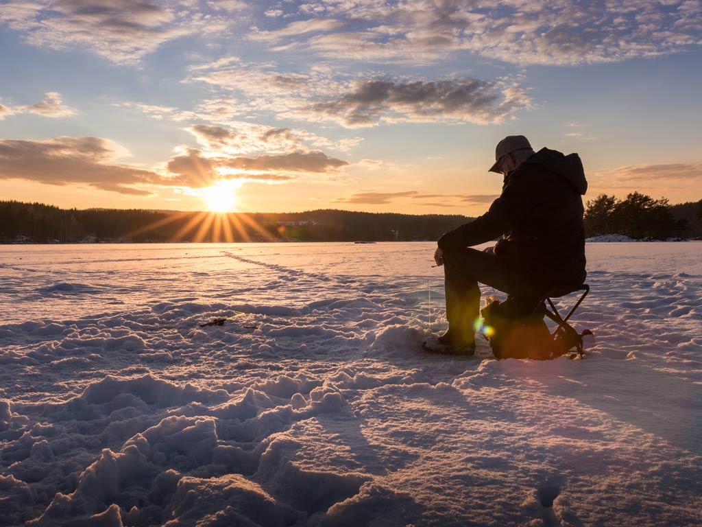 A beautiful sunset view of an angler sitting and ice fishing on the frozen lake