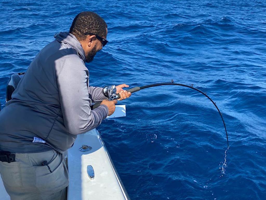 A side view of an angler struggling while bottom fishing from a charter boat