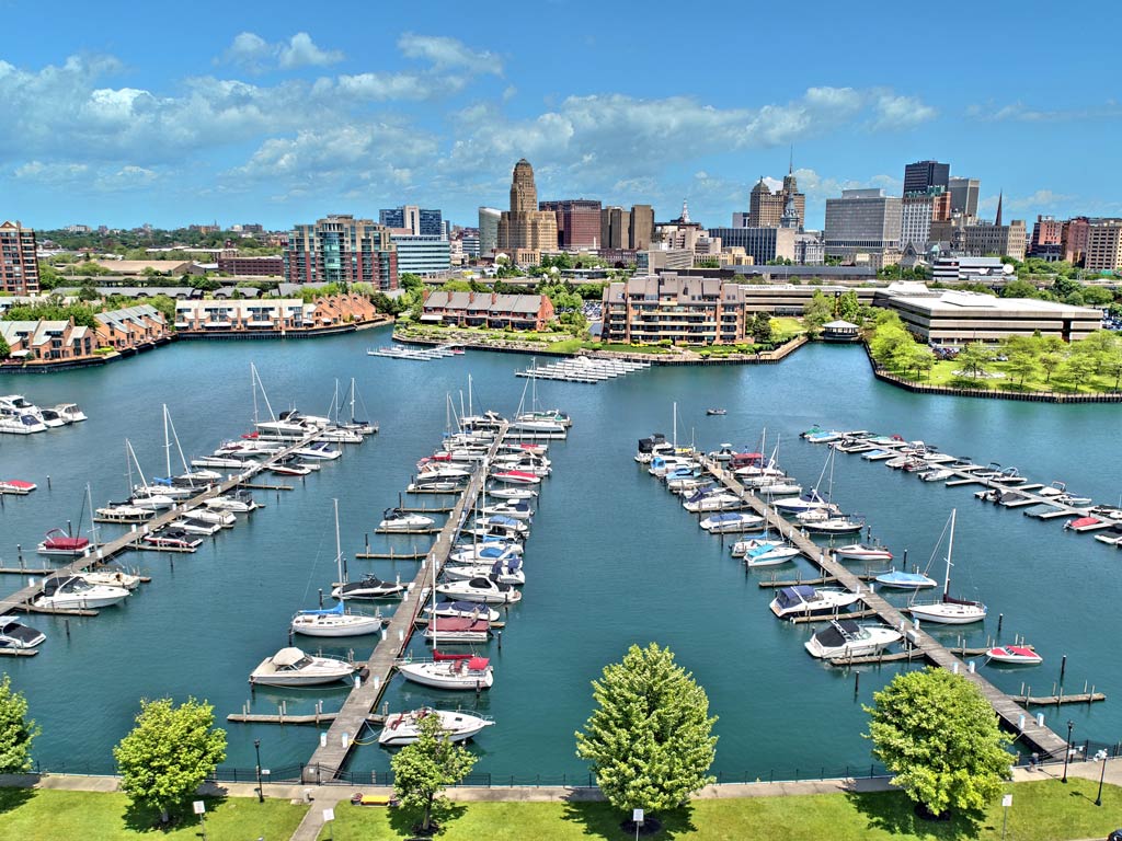 An aerial shot of Buffalo during a bright and sunny day, with a harbor populated with boats and charter operators in the foreground