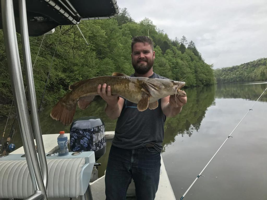 A fisherman on a boat, posing with a Catfish he caught.