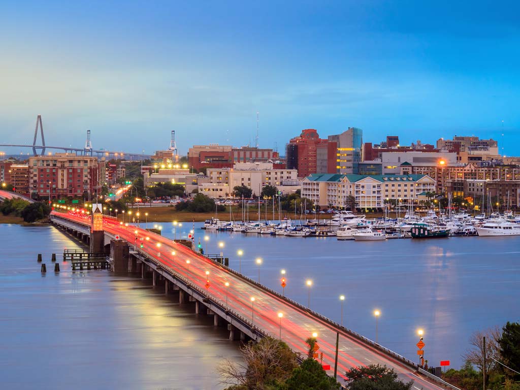 A sunset shot of a lit up bridge in Charleston, South Carolina, with the city skyline in the background.