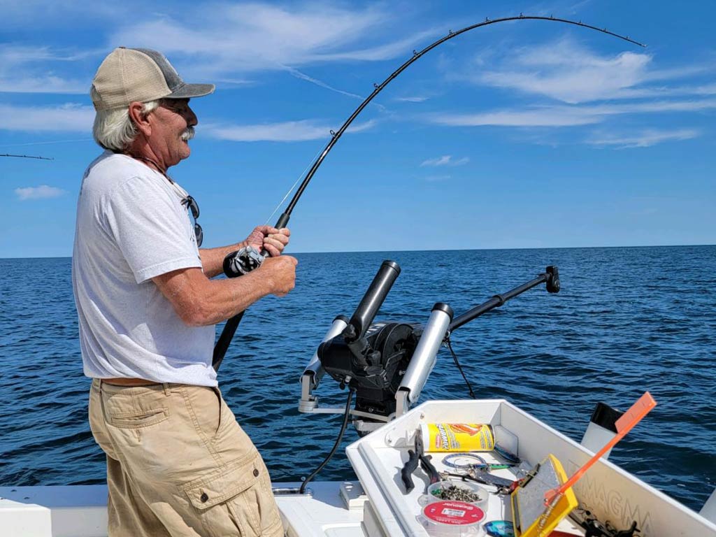 An older angler standing next to the bait and tackle while fishing from a charter boat and looking at the water