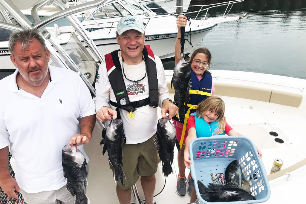 A family standing on a charter boat, holding their daily catch of Black Seabass