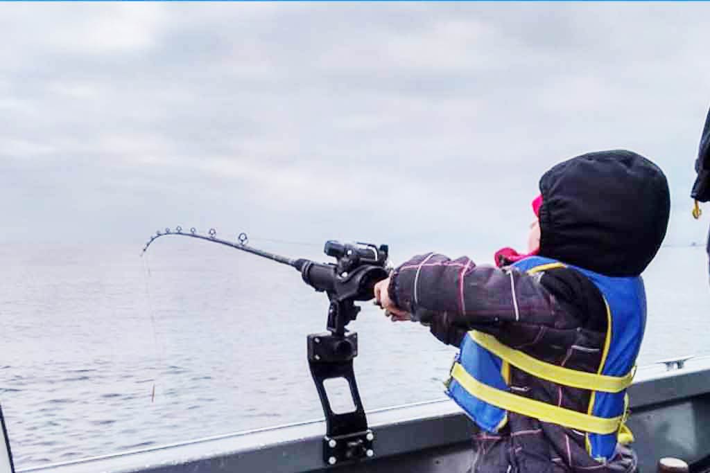 A child holding onto a rod with the fishing line in the water, grey skies in the background