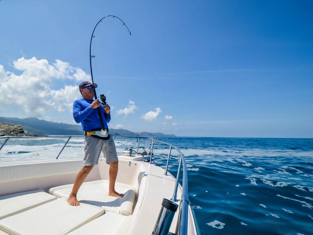 An excellent shot of an angler standing on a Coco fishing charter boat and holding a rod while bottom fishing in Costa Rica