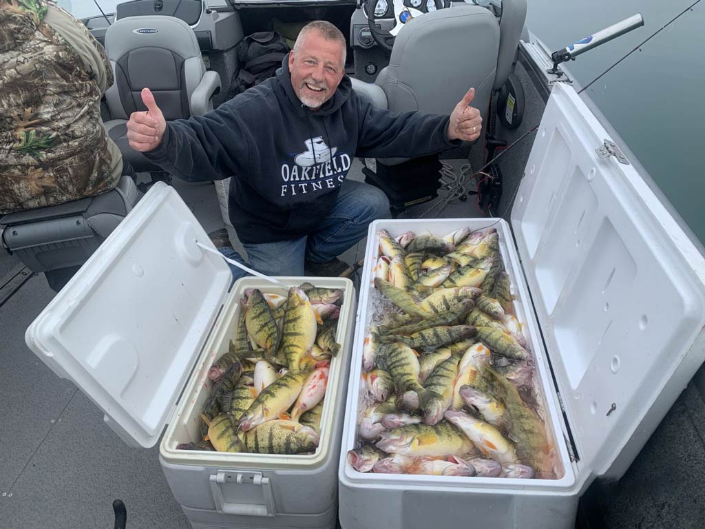 An angler posing happily next to two ice boxes full of Perch on a Buffalo fishing charter