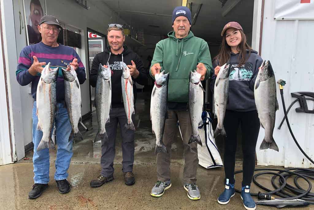 Four anglers standing on a dock, each holding two Coho Salmon