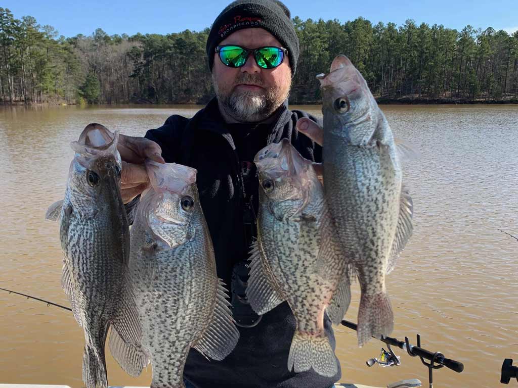 A man posing with four Crappies he caught while on a fishing trip.