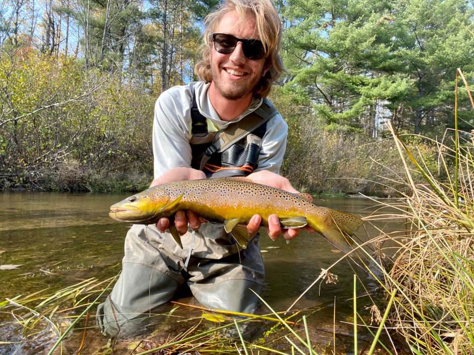 A picture showing a smiling wade angler holding Steelhead while kneeling on a river in Wisconsin