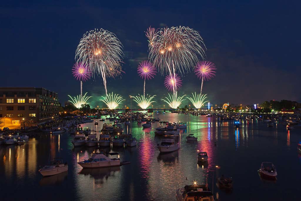 An view of boats on the Saginaw River with fireworks in the night sky