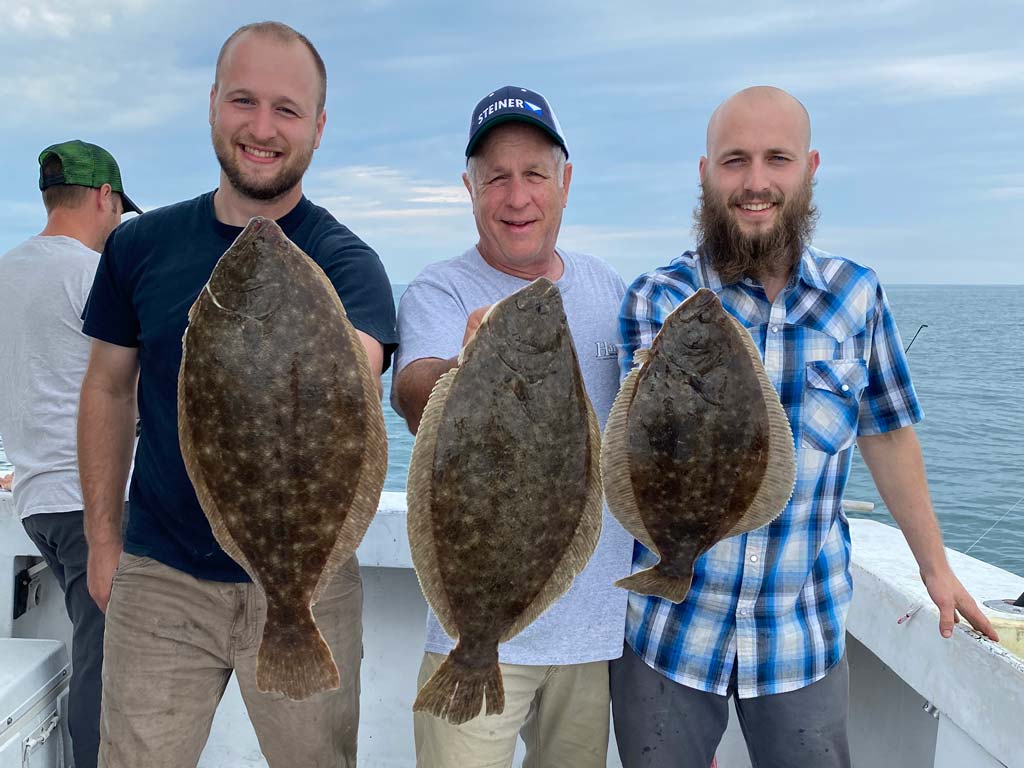 Three anglers standing next to each other, each holding a sizeable Flounder.