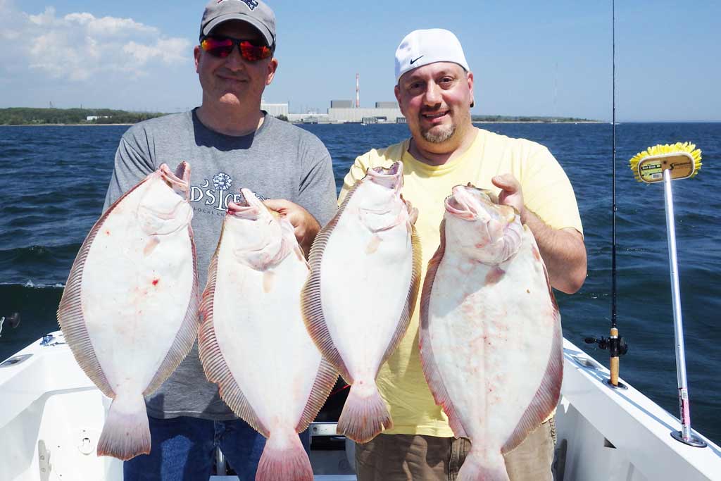 Two men in caps standing on a boat and holding two Flounder each