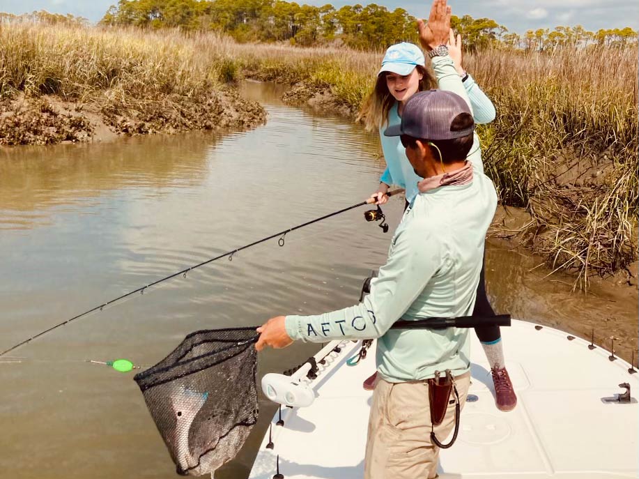 A picture showing a fishing guide high-fiving a female angler on catching a Redfish while standing on a fishing boat.