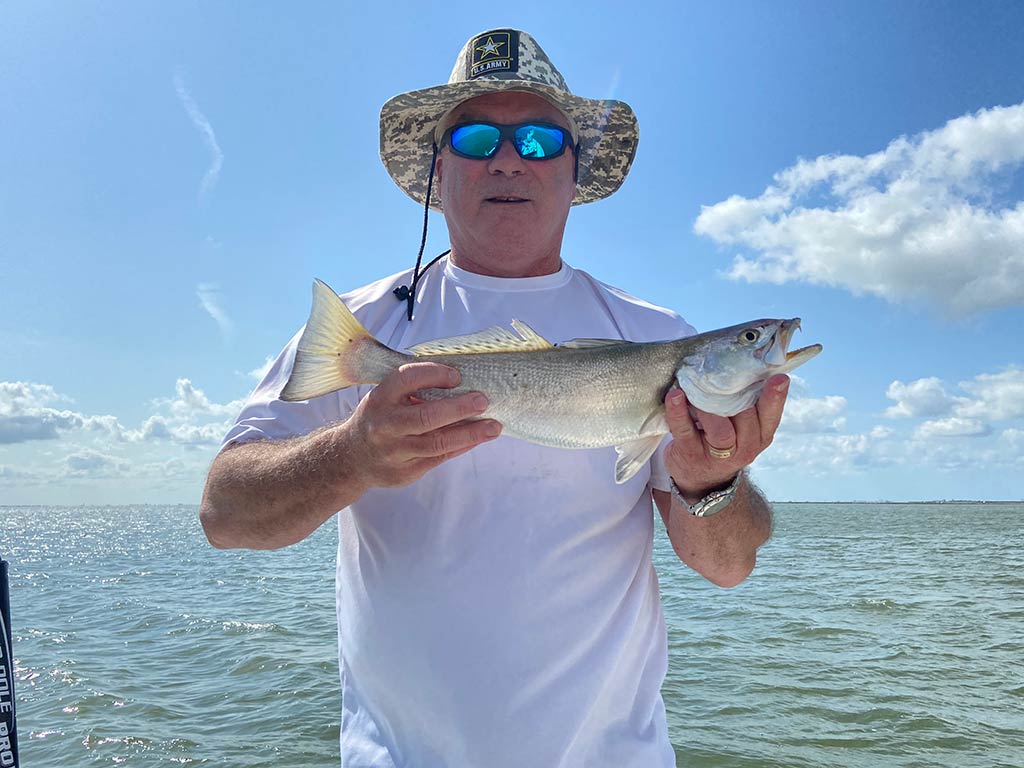 A smiling angler in a hat holding a Speckled Trout while on a fishing charter in Texas City