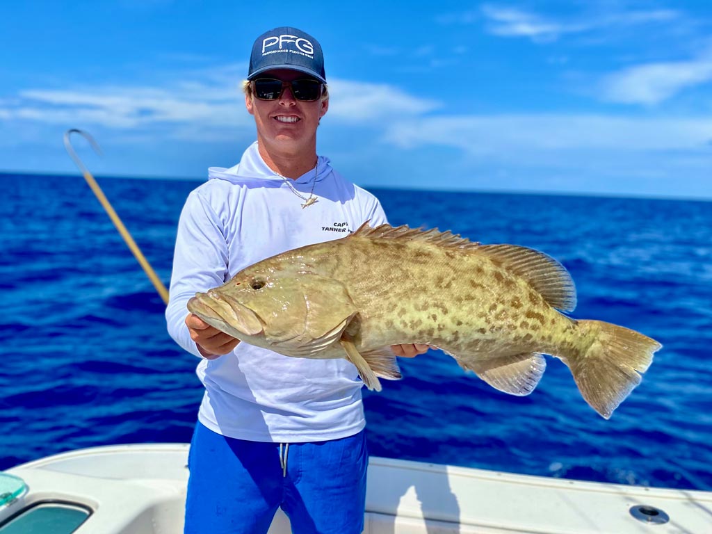 A man posing for a photo, holding a Gag Grouper he reeled in while deep sea fishing in Marco Island.