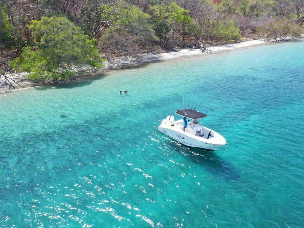 An aerial view of anchored Coco fishing charter boat near the beach in Costa Rica and a captain waiting for passengers to refresh in crystal-clear water