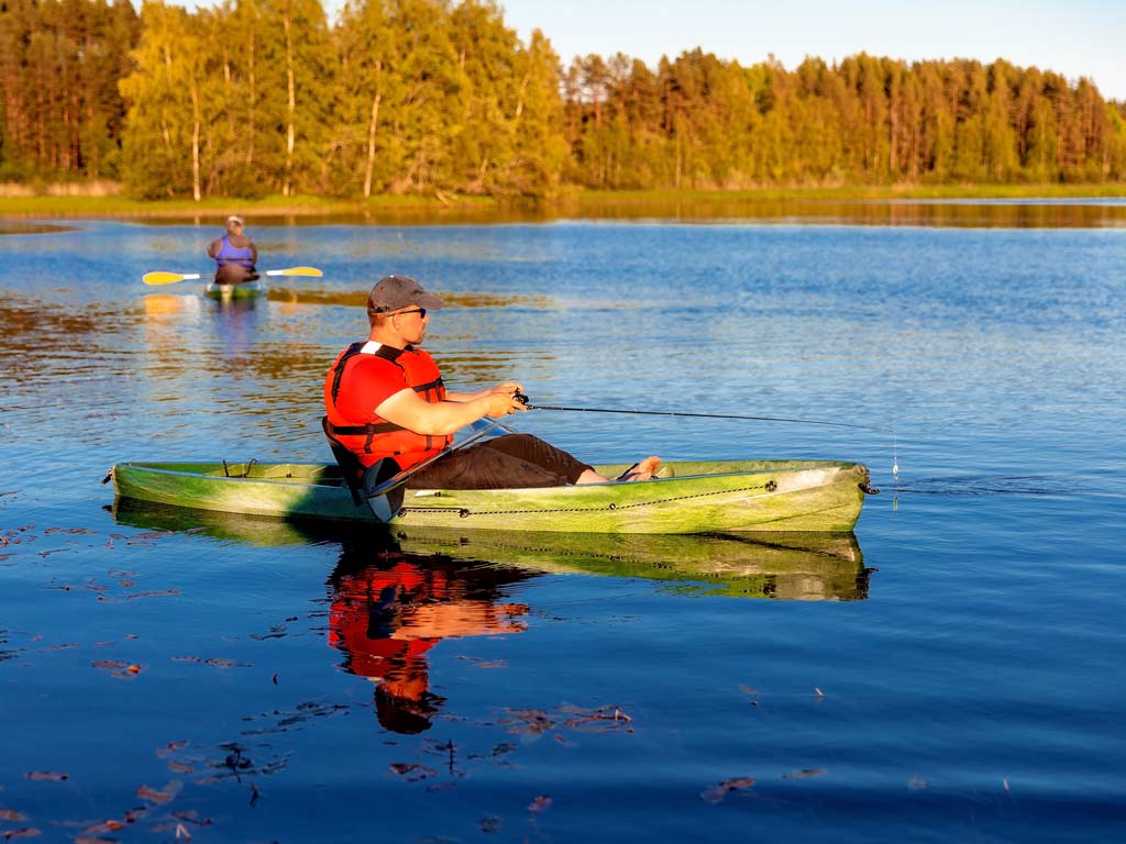 A man fishing from a kayak on a lake, with another angler in a kayak behind him.