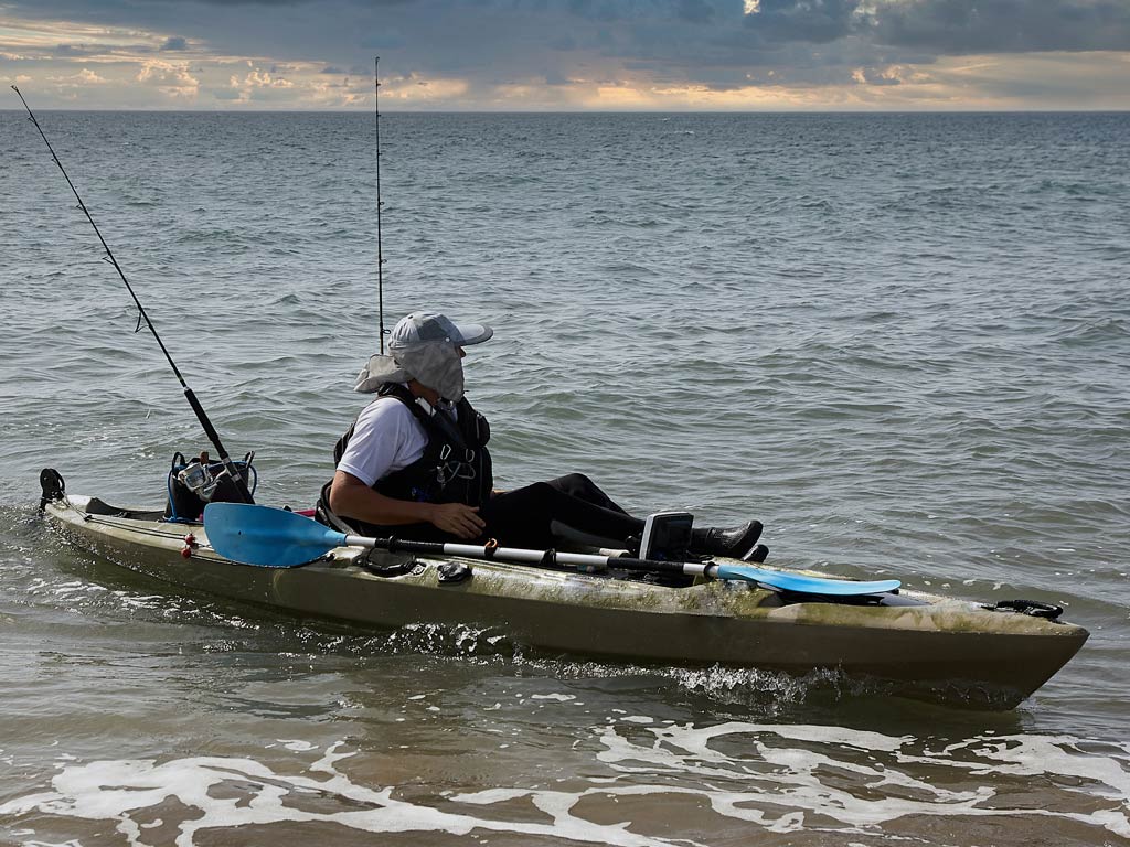 An angler sitting in a kayak and getting ready to fish in the bay on a cloudy day