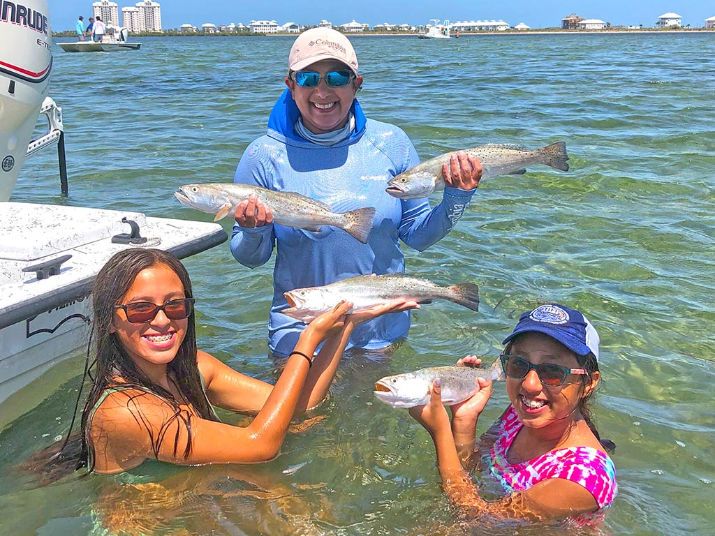 Three women in the water next to a charter fishing boat holding the Speckled Trout they caught