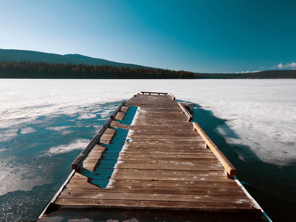 A magnificent shot of the wooden deck on a frozen Lake of the Woods in Oregon and a view of the evergreen forests and hills in the distance