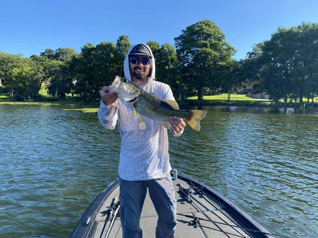 A fisherman standing on his boat, posing with a Bass he reeled in.