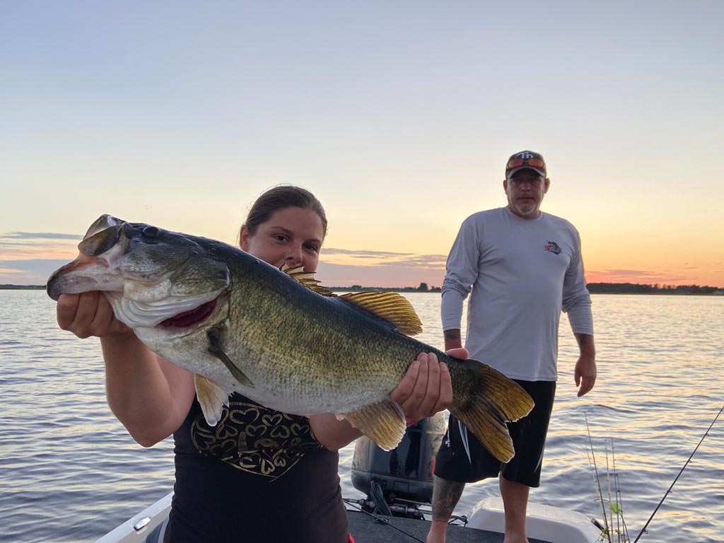 A young girl holding a big Largemouth Bass caught in Lake Ariana, with her fishing guide standing behind.