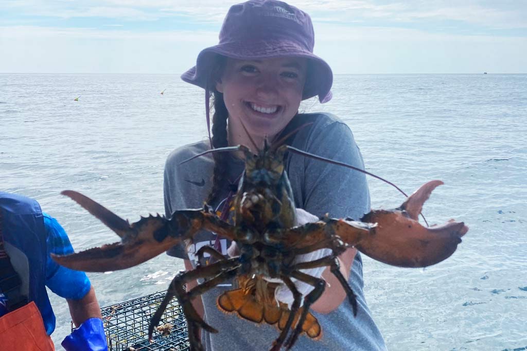 A smiling young woman in a hat showing off a Lobster to the camera