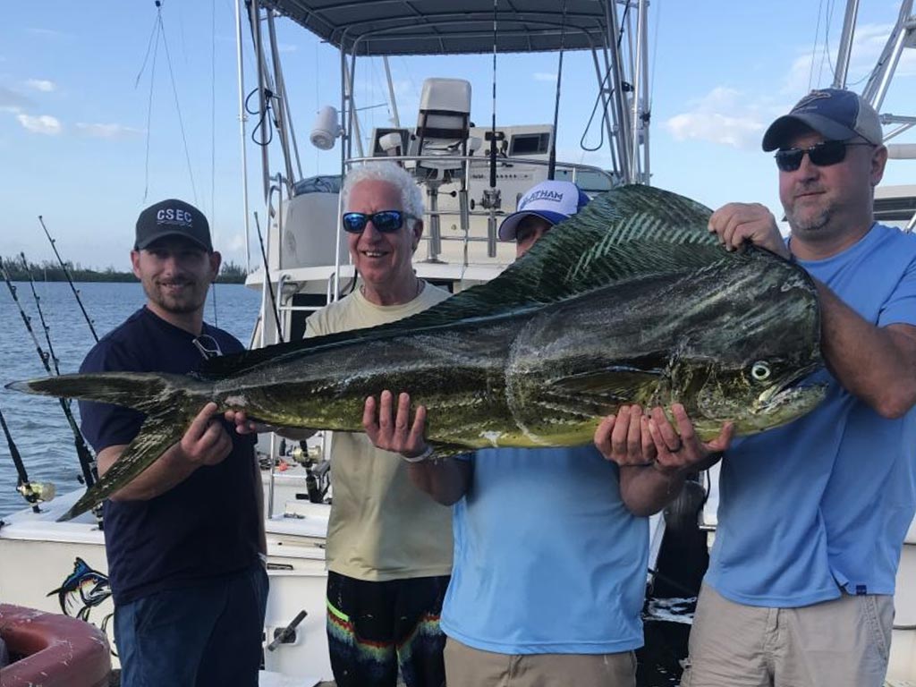 Four anglers on a boat holding up a big Mahi Mahi they recently caught on a fishing trip.