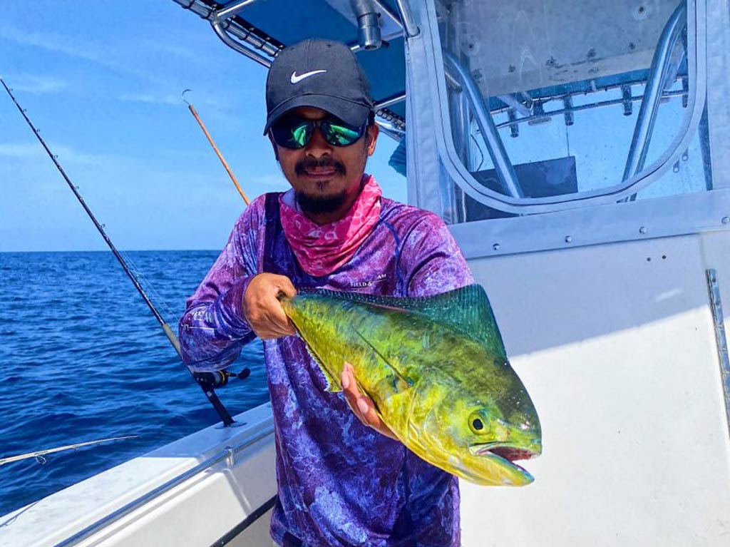 An angler posing with his small Mahi Mahi catch while standing on a Tarpon Springs fishing charter boat