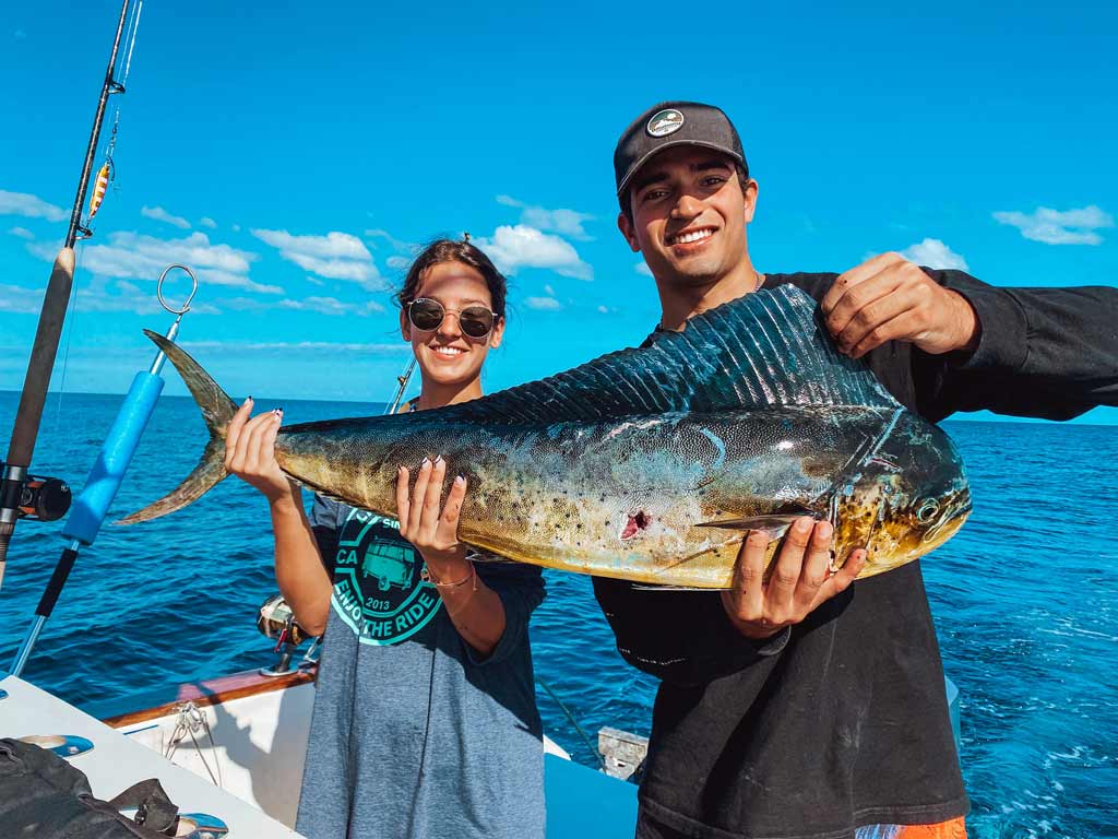 A man and a woman on a boat, posing for a photo with a big Mahi Mahi they caught during their peak fishing season in Costa Rica.