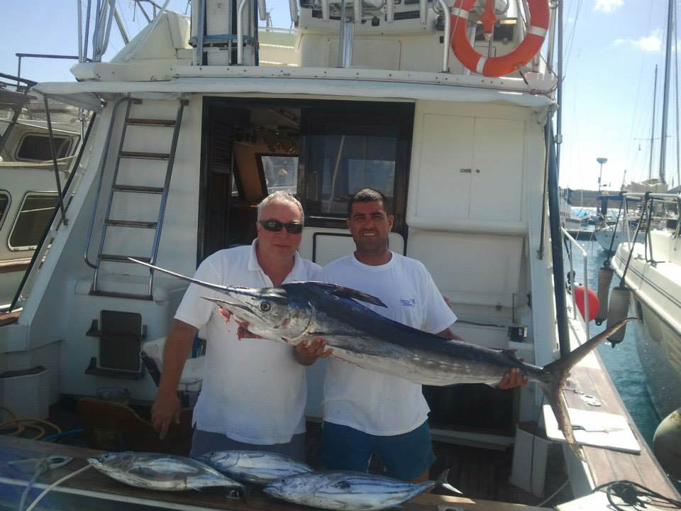 Two middle-aged anglers hold a Marlin on the deck of a Tenerife fishing charter