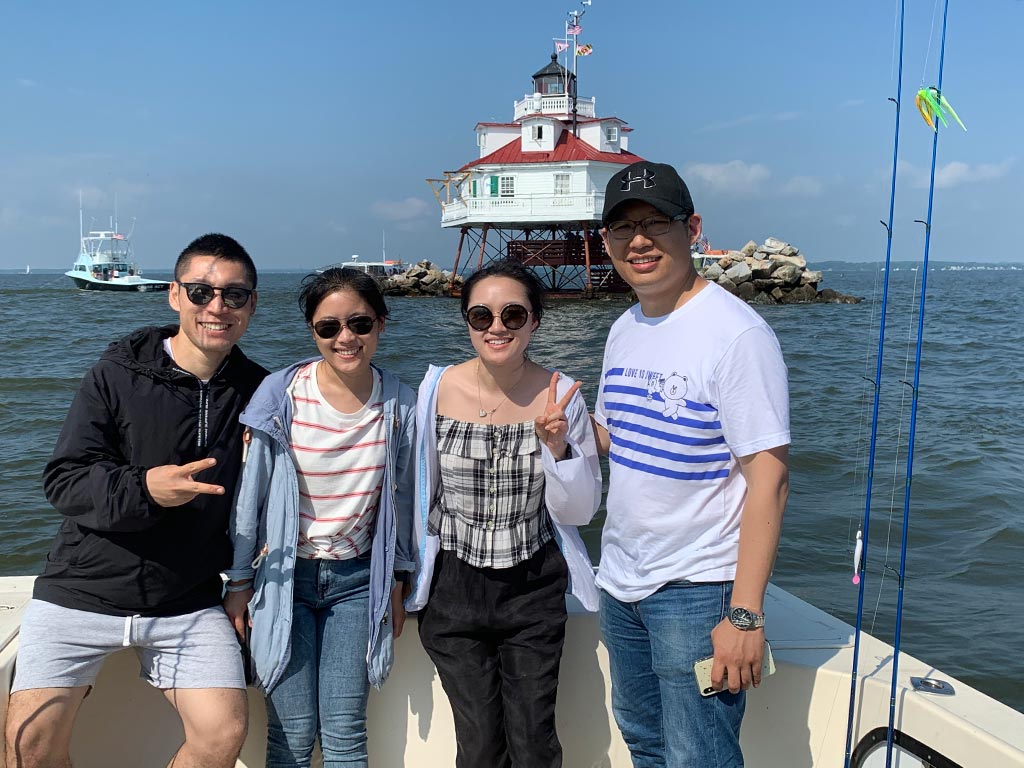 Four anglers posing for a photo while on a fishing trip in the Chesapeake Bay, with a lighthouse behind them