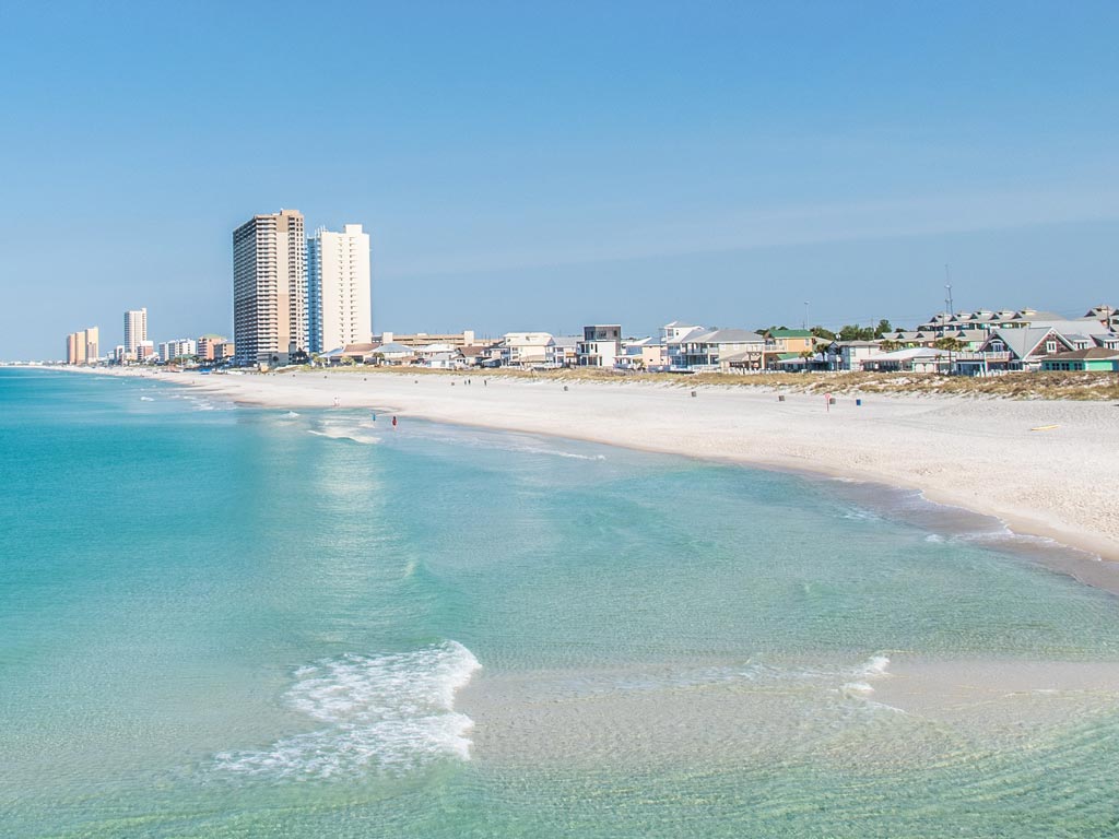 A photo of one of the beaches near Panama City Beach in Florida, with clear waters and buildings visible in the background.