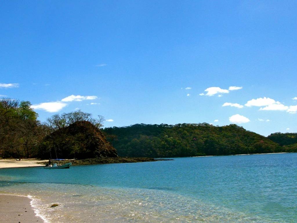 A photo of a wonderful sandy beach in Playas del Coco, small waves, a beautiful turquoise water, and a panga boat in distance