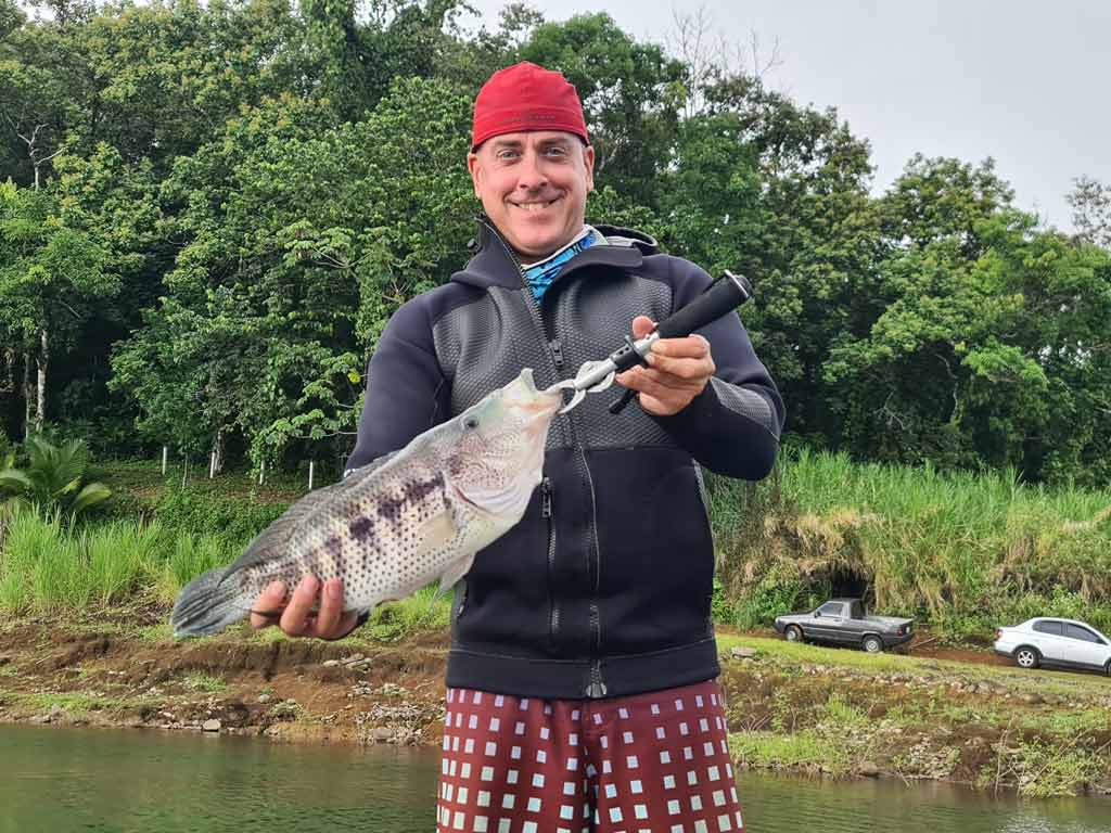 An angler holding a Rainbow Bass, also known as Guapote, which he caught fishing on Lake Arenal during the wet season.