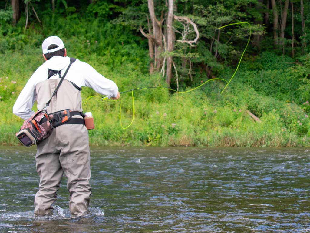 A fly fisherman wading in a shallow river and casting his line.