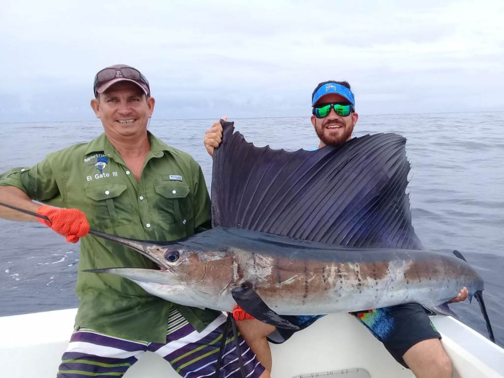 An incredible photo of two male anglers sitting on a charter boat and holding huge Sailfish caught while fishing in Playas del Coco offshore waters