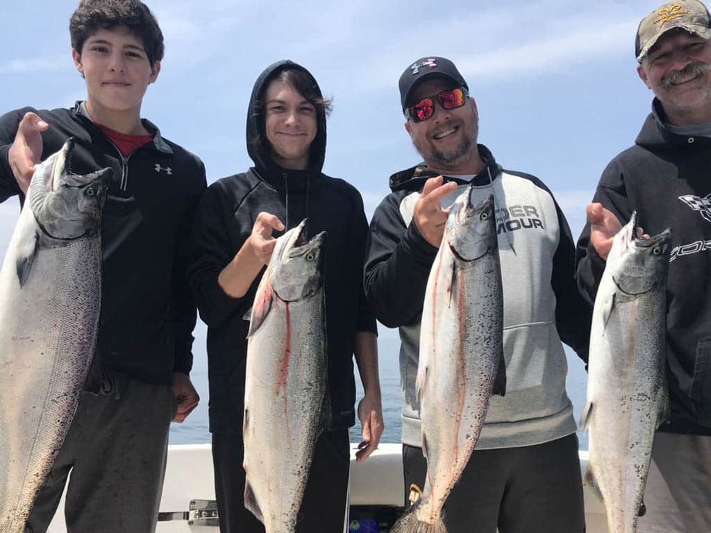 Four anglers standing on a fishing charter boat with a Salmon each in their hands