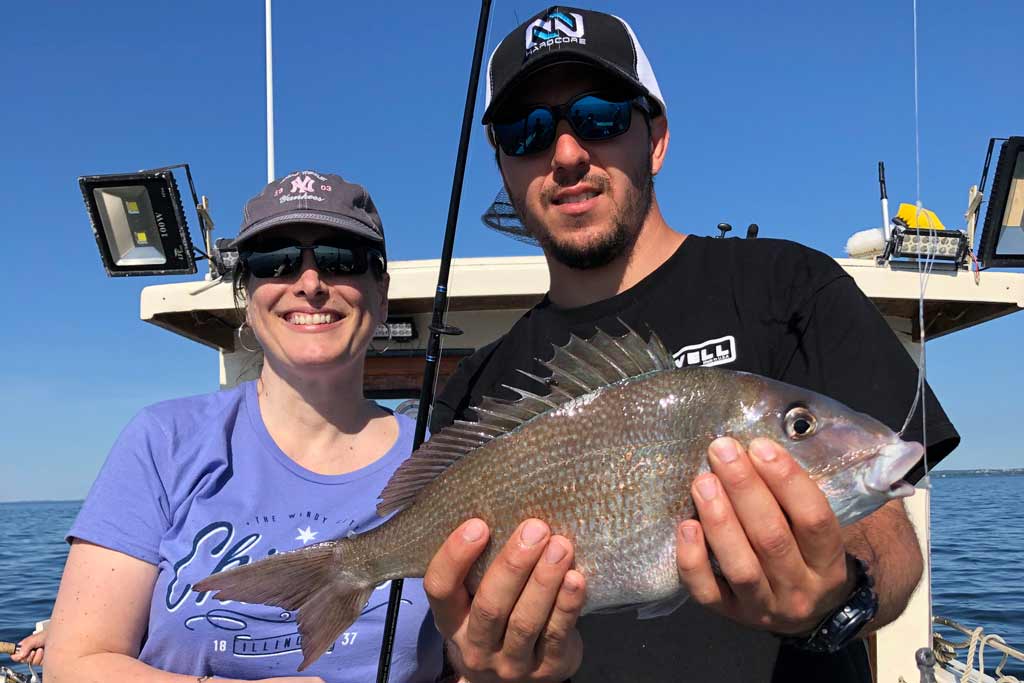 A man and a woman standing on a fishing boat, while the man is holding a Scup