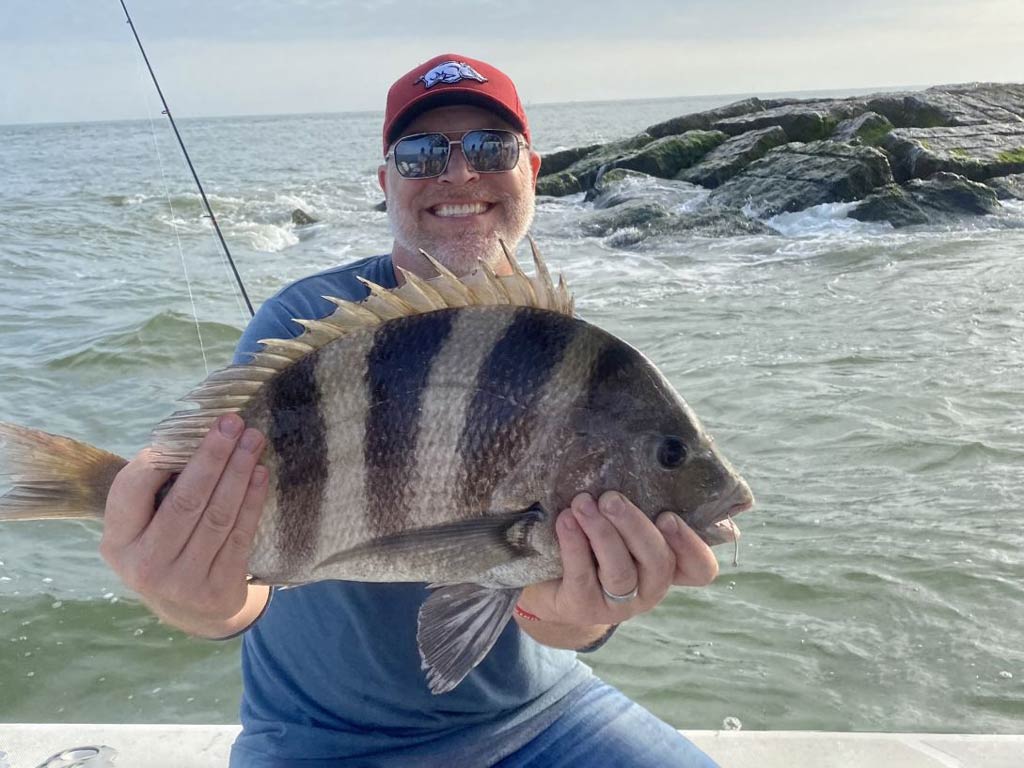 A happy angler sitting on a Trinity Bay fishing charter boat and holding big Sheepshead with both hands near the jetties