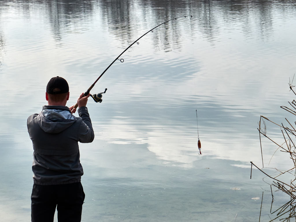 An angler casting his line from a lake shore.