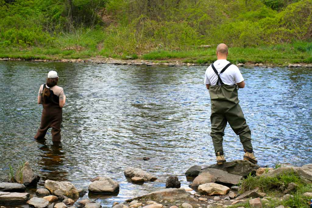 A rear-view image of a woman and a man wading in a small river in Connecticut