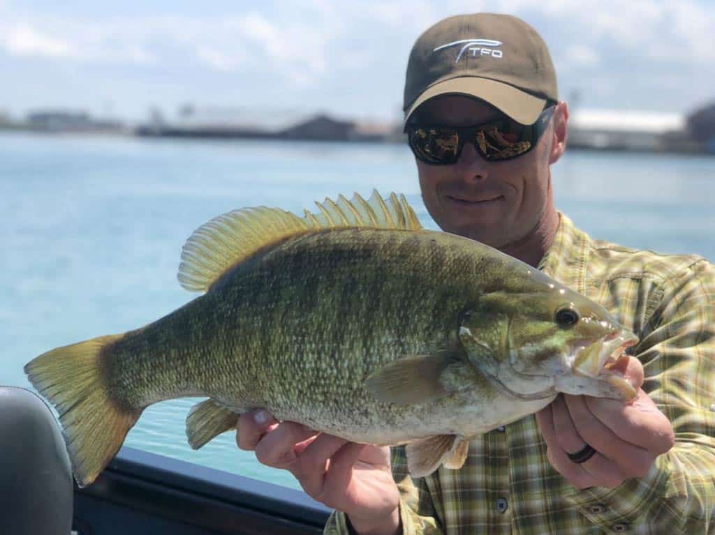 An excellent shot of a Smallmouth Bass caught in Buffalo, with an angler showing it off while standing on a charter boat