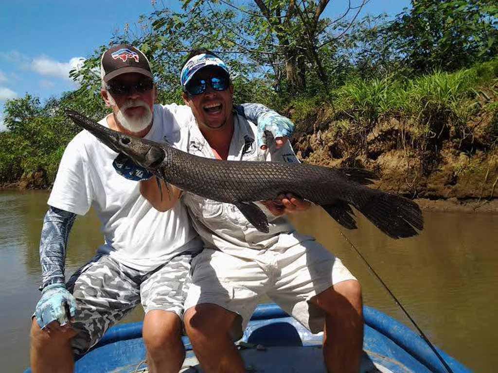 A pair of anglers on a small river boat, posing with a Tropical Gar they reeled in.